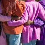 The backs of a group of four women with arms wrapped around each other.